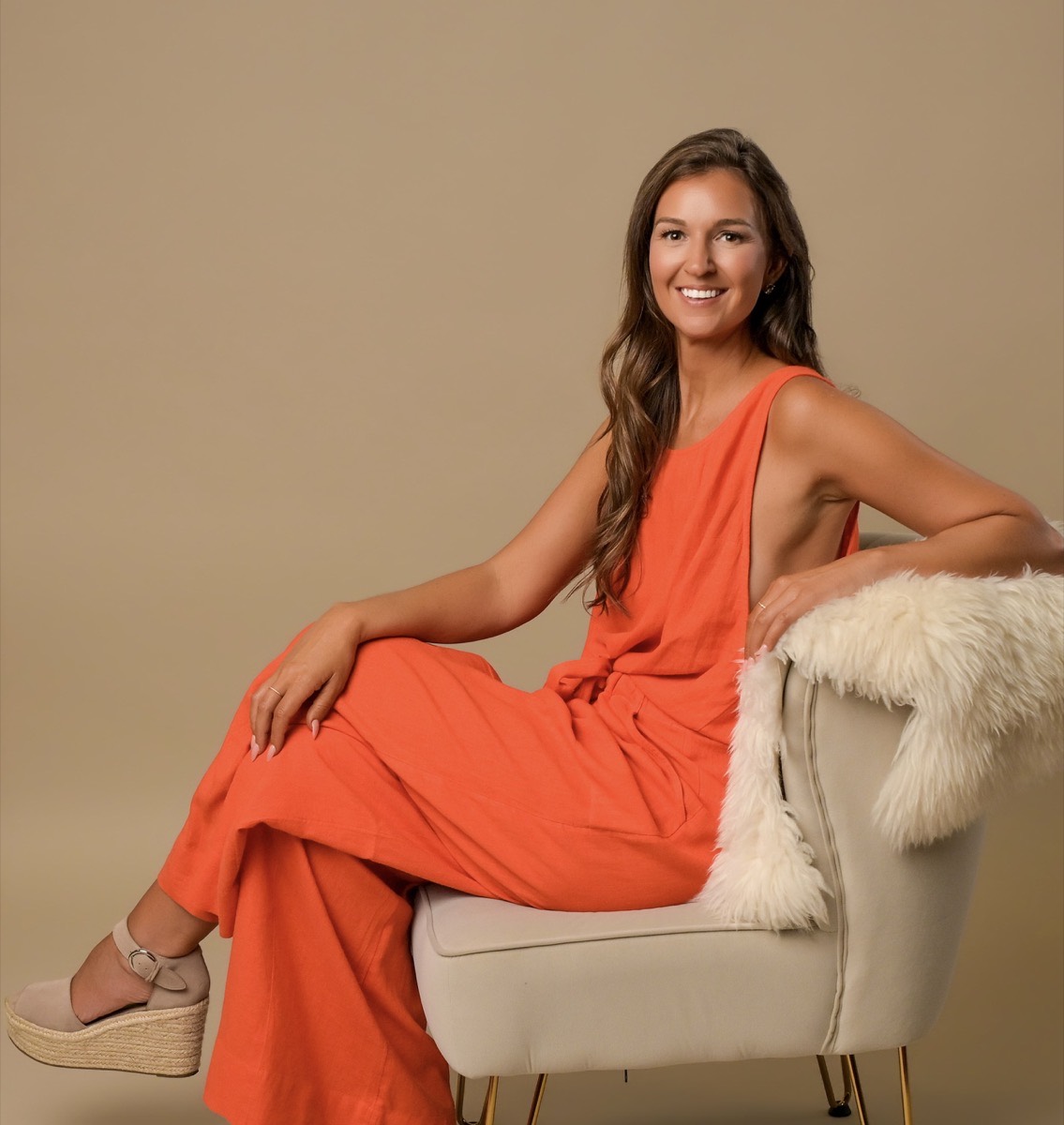 Rebecca in an orange jumpsuit, smiling in a studio portrait